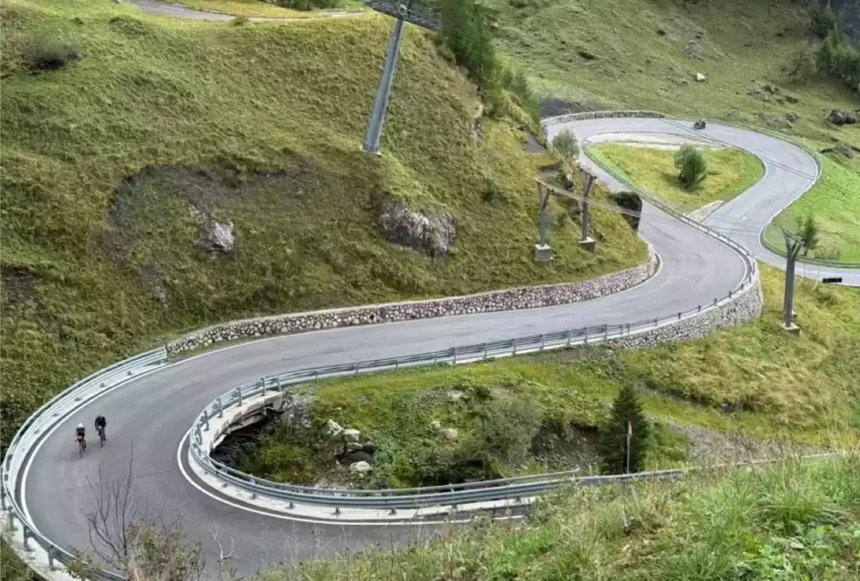 Two cyclists climbing in the dolomites on a twisty road.
