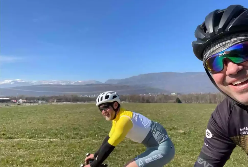 Two cyclists riding on a sunny day. there are mountains in the distance.