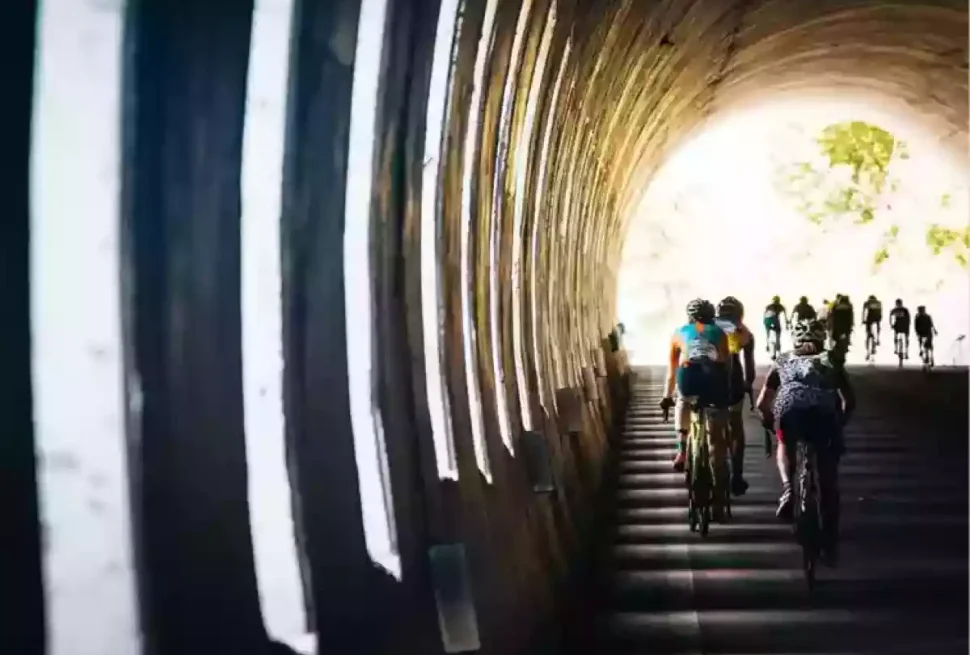 Cyclists in a tunnel with bright light at the end and shafts of light coming in from the left