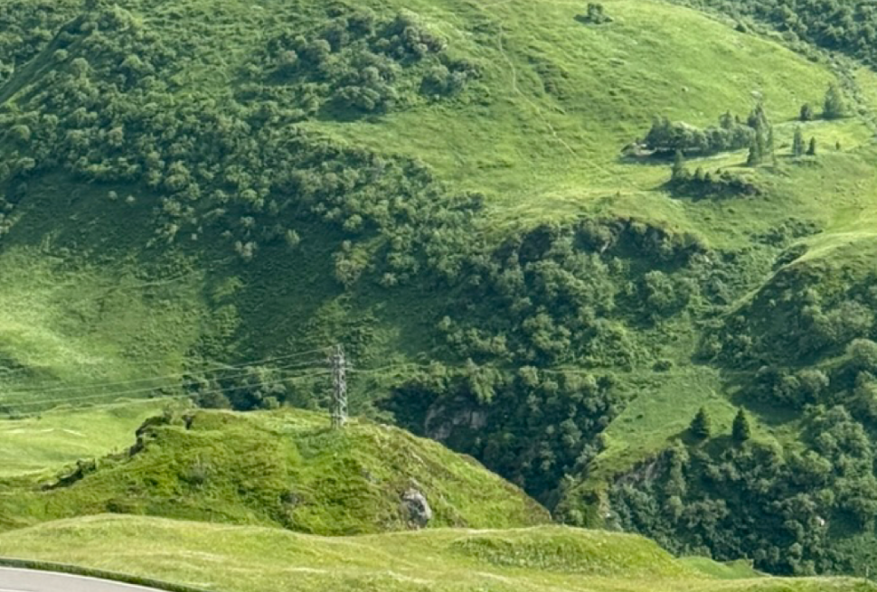 A view of the mountainside with a cyclist descending the road at the bottom of the image.