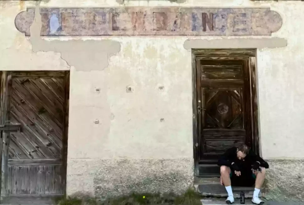 Tired cyclist sitting down outside abandoned house