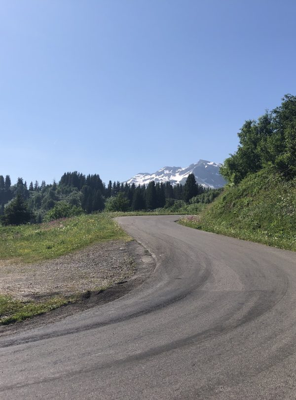 A female cyclist riding up a deserted mountain road with snowy mountains in the background
