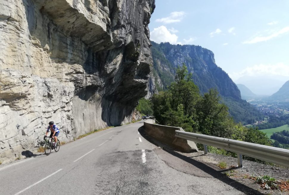 A cyclist riding next to a cliff face with views back down the valley